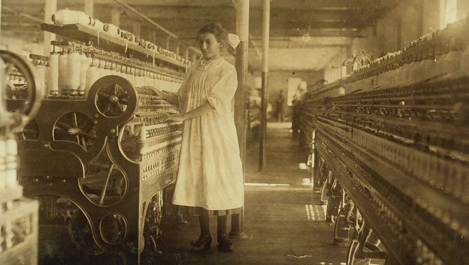 Une jeune femme devant une machine de filage à gauche et à droite un alignement de machines de filage.