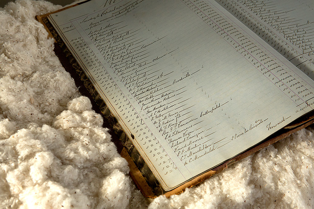 Livre ouvert avec une écriture anglophone relié au centre par un fil, couché sur du coton brut.