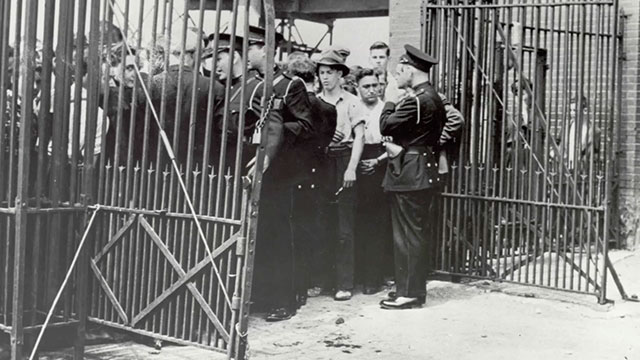 Strikers and police in front of the open gate of the factory.